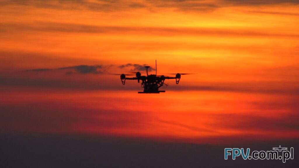 Dron w powietrzu na tle zachodzącego słońca.