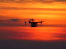 Dron w powietrzu na tle zachodzącego słońca.